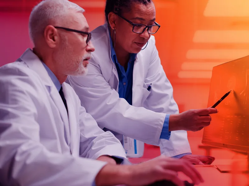 Two medical researchers in lab coats analyzing brain scans on a computer monitor during a clinical study.