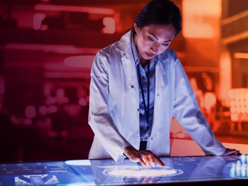 Female researcher in a lab coat analyzing a brain scan on an interactive digital display table.