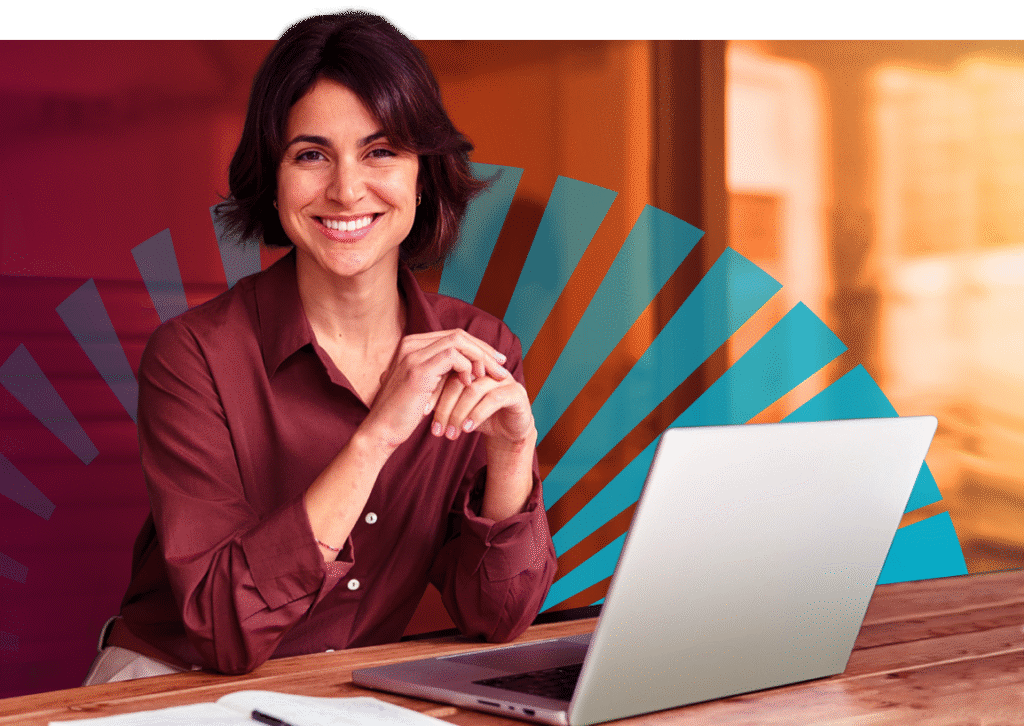 Smiling woman with dark hair in a maroon blouse sits at a wooden desk with an open laptop, hands clasped, against a warm orange background overlaid with a semi-transparent teal fan-shaped graphic; a notebook and pen are in the foreground.