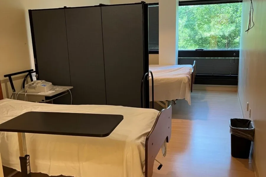 Patient room with privacy screen dividing two beds and an overbed table.