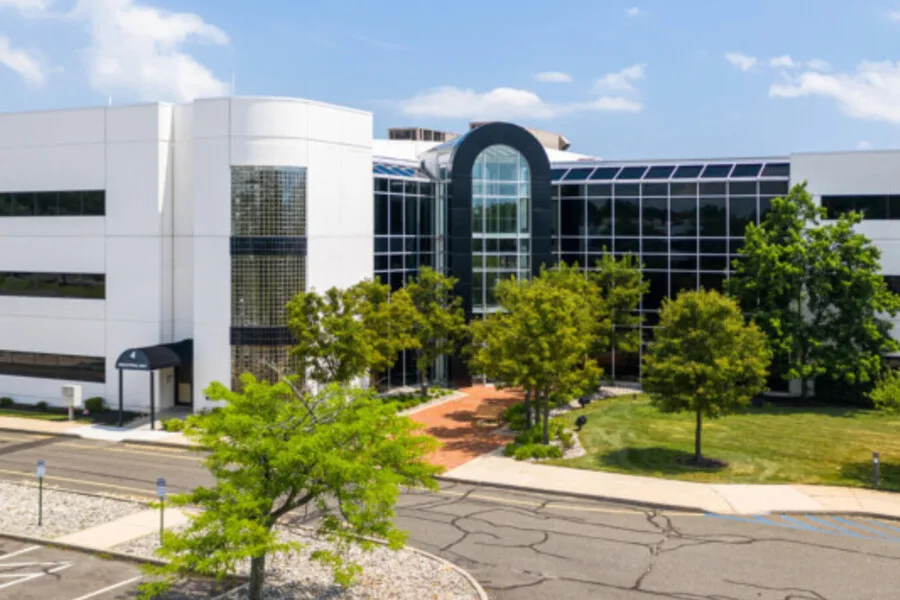 Exterior view of modern office building with central glass atrium and surrounding trees.