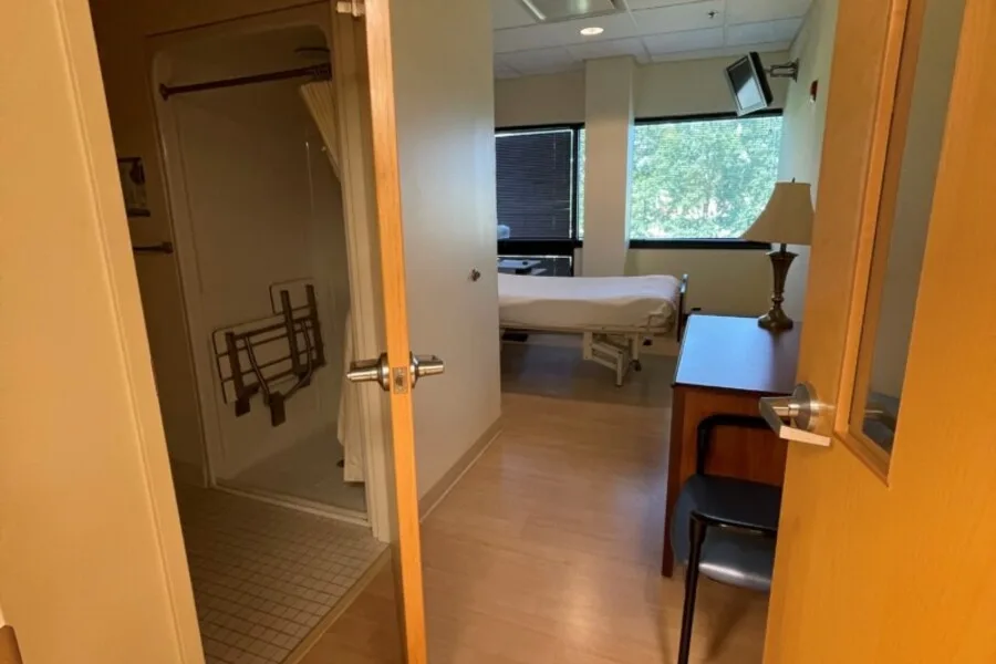 Patient room entry showing accessible shower and hospital bed by window.