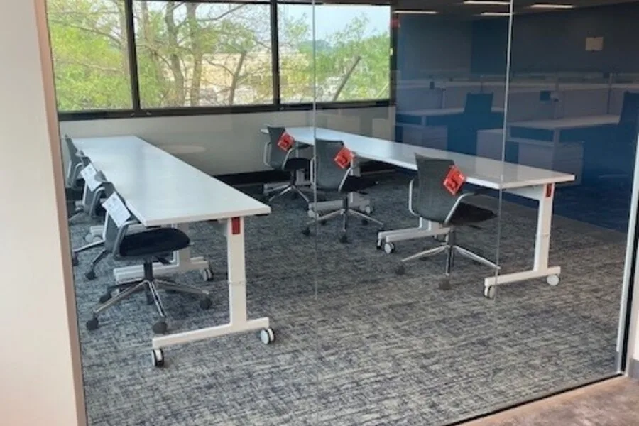 Glass-walled training room with long white tables on casters and task chairs.