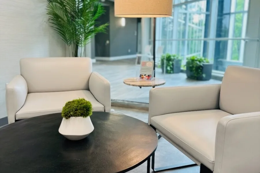 Modern lobby seating with two white armchairs, round black coffee table, and small plant.