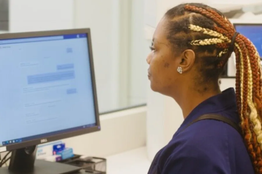 Staff member with braided hair working at a desktop computer in a clinic.