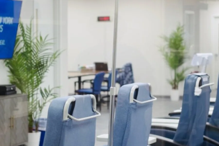 Clinic area viewed through glass with blue recliner chairs and plants.