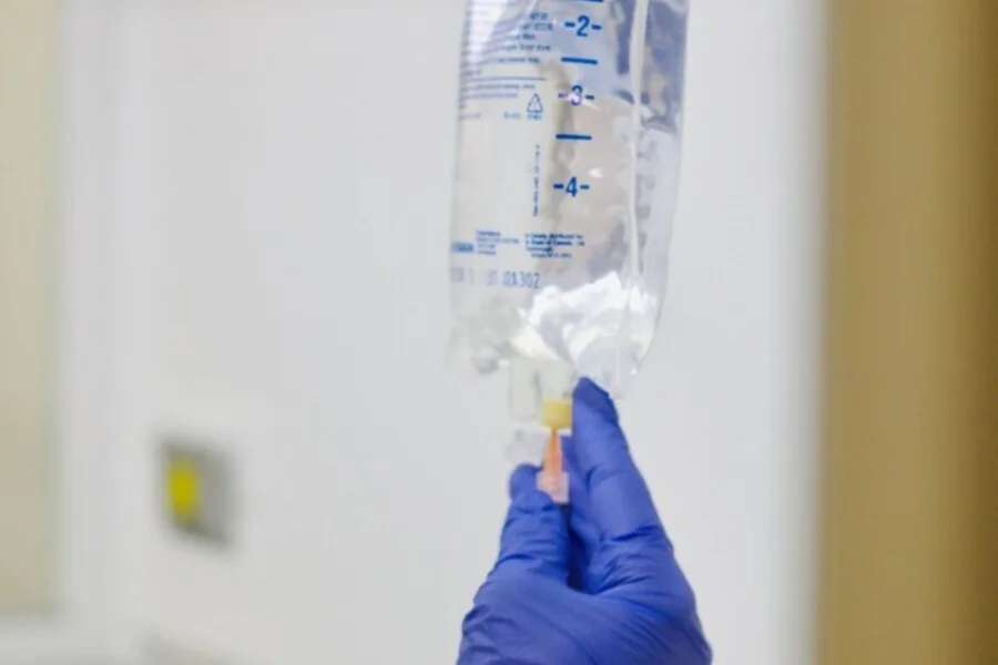 Gloved hand holding a clear IV bag, measurement markings visible