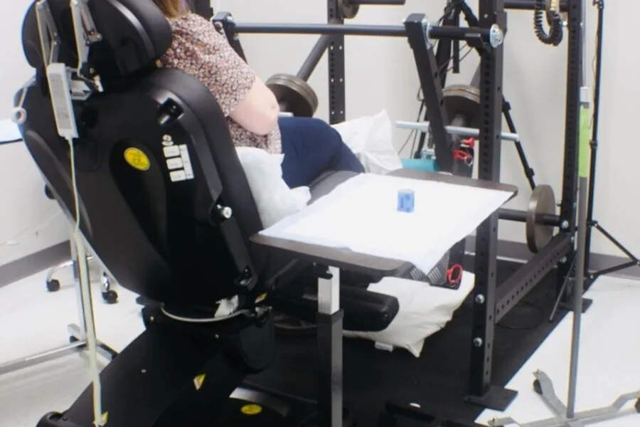 Research participant seated in a clinical leg-press/exercise rig with an IV line and side tray.